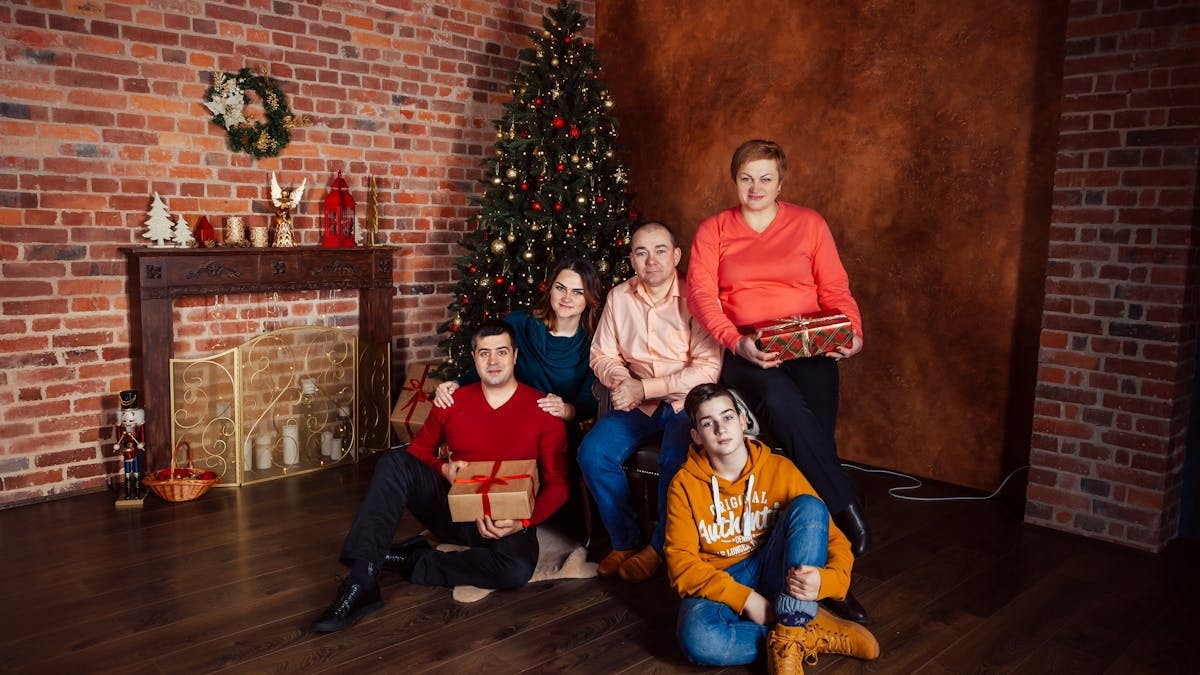 A family posing with Christmas gifts by a decorated tree indoors, exuding holiday warmth.