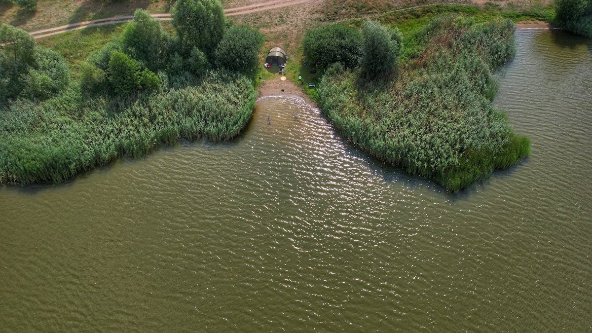 Aerial shot of a tent by a serene lakeside surrounded by lush greenery.