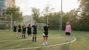Women's soccer team practices drills on a sunny outdoor field with coach observing.